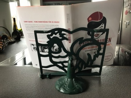 Der Hahn hält das Kochbuch.
